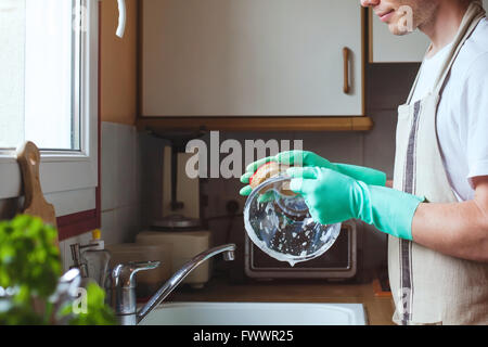 man washing dishes in the kitchen sink at home, close up of hands with sponge and soap, housework Stock Photo