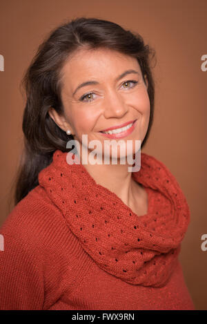 Smiling middle aged woman in front of brown background Stock Photo