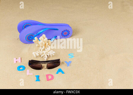 Pair of flip flops, sunglasses, pieces coral and coloured letters spelling holidays on a sand background Stock Photo