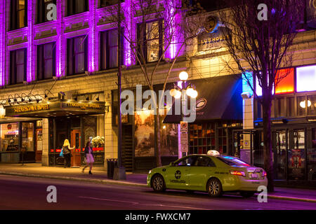 Taxicab waiting for customer outside Strathcona hotel and pub with women on street at night -Victoria, British Columbia, Canada. Stock Photo