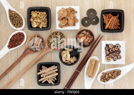 Chinese herbal medicine selection with I ching coins, mortar with pestle and chopsticks over light oak background. Stock Photo