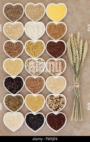 Grain and cereal food selection in heart shaped porcelain bowls over rough brown paper background with wheat ears. Stock Photo