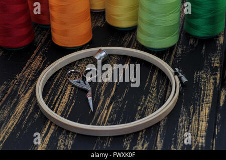 Hoop, scissors and colored threads for sewing and embroidery on the background of a wooden black table Stock Photo