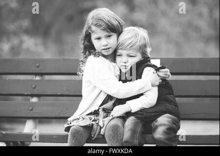 Brother and sister hugging on a park bench Stock Photo