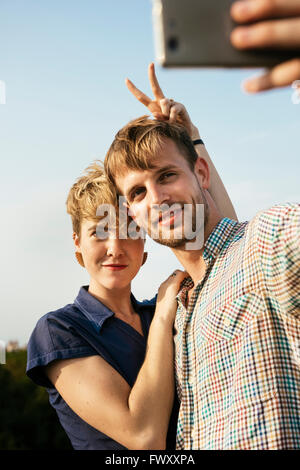 Germany, Berlin, Young couple hugging and taking selfie with smart phone