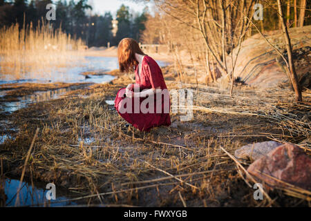 Finland, Varsinais-Suomi, Young woman crouching in wetlands