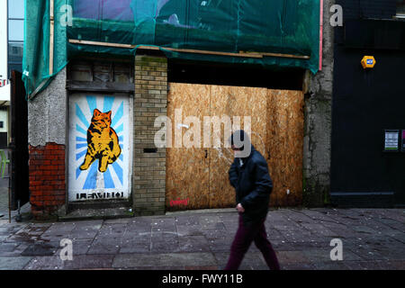 Young man wearing hooded top walking past cat mural on abandoned building in Womanby Street, Cardiff, South Glamorgan, Wales, UK Stock Photo