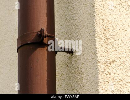 Old rusty brown gutter on the yellow wall. Stock Photo