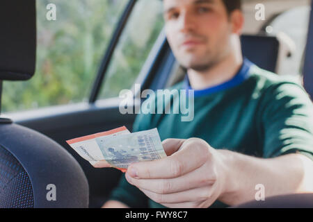pay by cash in taxi, closeup of hand of passenger giving money to the driver in car Stock Photo