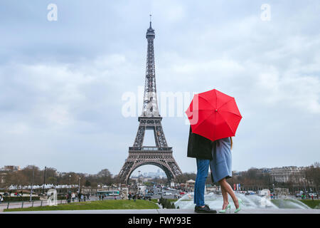 honeymoon in Paris, couple kissing behind red umbrella against Eiffel tower Stock Photo