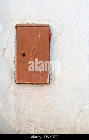 Rusty brown iron doors of switchboard on white wall. Stock Photo