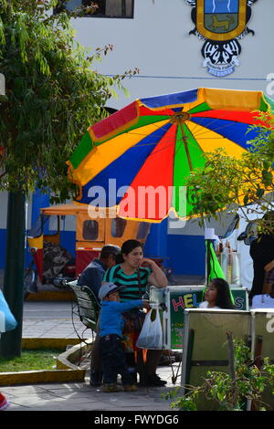 A woman with child sells sweets from a vendor cart in the Plaza de Armas in the city of Urubamba Peru. Stock Photo