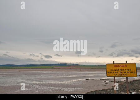 The uncovered causeway across from Lindisfarne (Holy Island)  to mainland at low tide, Northumberland, England with sign warning Stock Photo