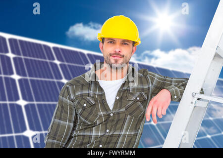 Composite image of smiling handyman in overalls leaning on ladder Stock Photo