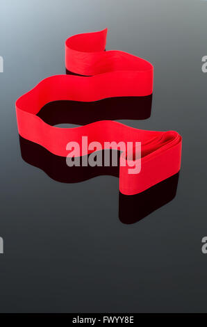 Curled red ribbon isolated on black white gradual background, elegant celebration symbol. Stock Photo