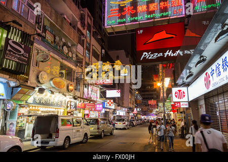 People and cars at a street full of shops and restaurants in Tsim Sha Tsui, Hong Kong, China, at night. Stock Photo