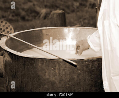 cheesemaker checks with hand the milk's temperature inside the large copper cauldron during the milk curds with rennet and whey Stock Photo