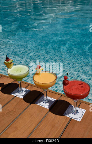 Red yellow and green cocktails on a wooden deck next to a pool Stock Photo