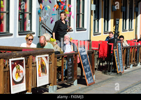 Simrishamn, Sweden - April 1, 2016: Some guests are dining outside on this fine spring day. The female attendant keeps an eye on Stock Photo