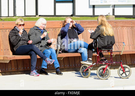 Simrishamn, Sweden - April 1, 2016: Four persons of different age are seated together eating ice cream in the sunshine. One sit Stock Photo