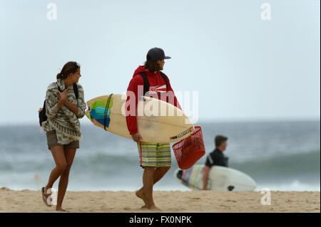 Young couple watch the surf as they cross the sand surfing in the Algarve Praia do Zavial Stock Photo