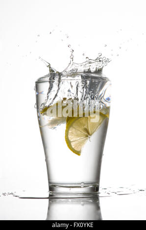 Three lemons are falling into the glass of water. Stock Photo