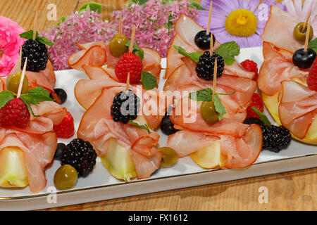 Galia melon with ham, garnished with raspberries, blueberries, blackberries and olives on a plate Stock Photo