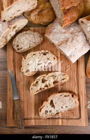 A variety of fresh baked loaves of bread, with slices on a wood cutting board. Top view in Vertical format. Stock Photo