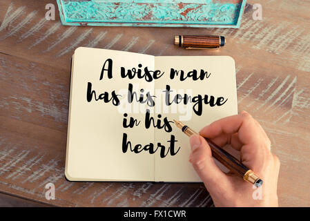 Retro effect and toned image of a woman hand writing on a notebook. Handwritten quote A wise man has his tongue in his heart as inspirational concept image Stock Photo