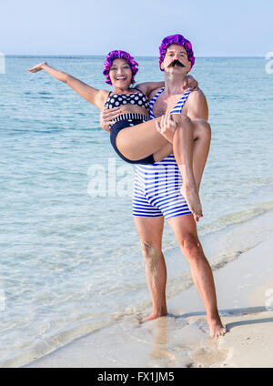 Man in swimsuit holding in his arms a woman in a swimsuit on the sea beach Stock Photo