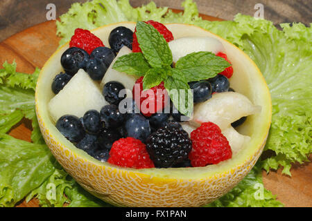 Melons bits, raspberries, blackberries and blueberries in a halved and hollowed Galia melon, garnished with mint Stock Photo