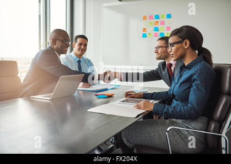 Two young multiracial business teams reaching an agreement in negotiations stretch across the table in the conference room to sh Stock Photo