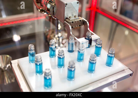 Robotic mechanical arm is manipulating chemical tubes full with blue substance in a medical laboratory during a test. Stock Photo