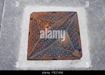 Close up of old, slightly rusty, cast iron drain cover in a concrete pavement Stock Photo