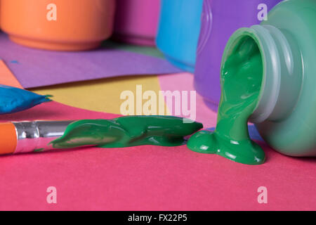 green paint spilling from container, blue, orange and red colors in background Stock Photo