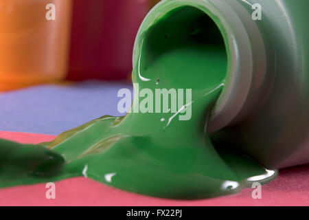 green paint spilling from container, blue, orange and red colors in background Stock Photo