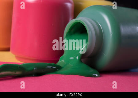 green paint spilling from container, blue, orange and red colors in background Stock Photo