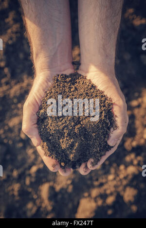 Farmer holding pile of arable soil and examining its quality on fertile agricultural land, male agronomist preparing land for ne Stock Photo