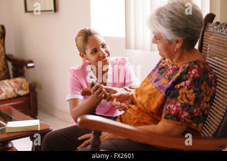 Old people in geriatric hospice: elderly lady having eyesight problems viewing the screen of mobile phone. A nurse helps the sen Stock Photo