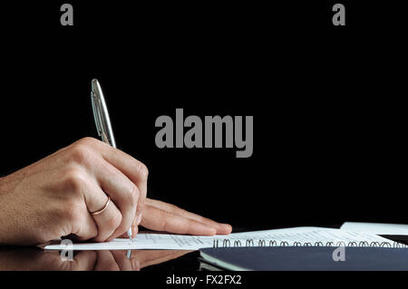Close up Human Hand Signing on Formal Paper at the Table. Black Background. Stock Photo