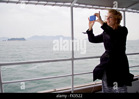 U.S Ambassador to Japan Caroline Kennedy takes a cell phone photo during the boat trip to Miyajima Island April 10, 2016 in Hiroshima, Japan. Kennedy is accompanying Secretary of State John Kerry for the annual G-7 Foreign Ministers meeting. Stock Photo