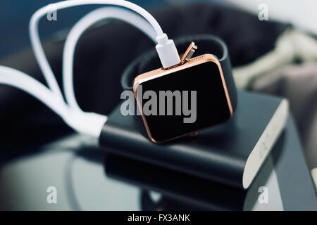 Smart wrist watch charging from a travel powerbank charger. Travel and stay connected to the media networks form anywhere you want. Stock Photo