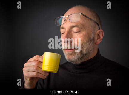 Enjoying morning espresso coffee - 60 years old  man with a beard and glasses - a headshot against a black background Stock Photo