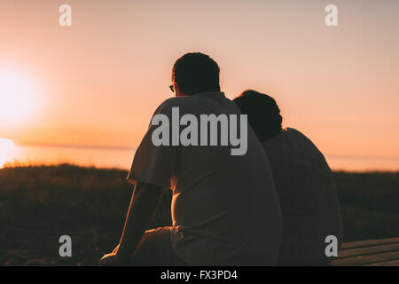 Side view a married couple a silhouette sitting on a bench. Stock Photo