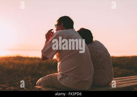 Side view a married couple a silhouette sitting on a bench. Stock Photo