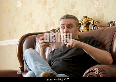 surprised man looking at cell phone while sitting on a sofa Stock Photo