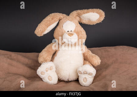 Stuffed toy rabbit resting on brown pillow Stock Photo
