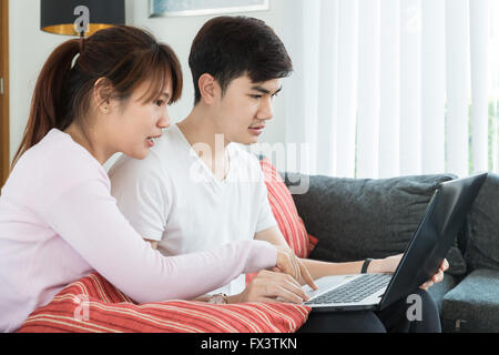 Asian young couple surfing on internet with laptop. Modern white apartment in background Stock Photo
