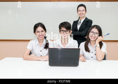 Asian teacher assisting student using laptop at desk in classroom Stock Photo