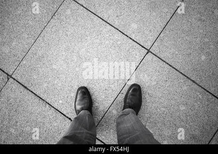 Feet of an urbanite man in black new shining shoes standing on gray cobblestone tiling